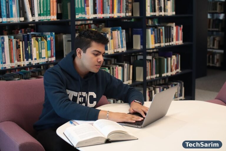 Student studying in a library with a laptop and textbooks