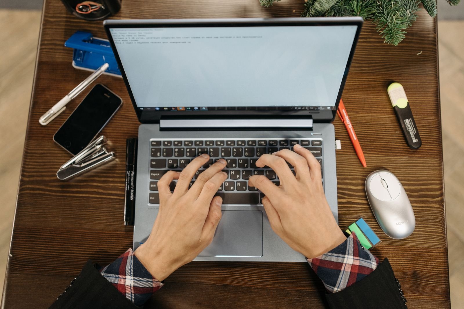 Overhead view of hands typing on a laptop surrounded by notebooks and office supplies