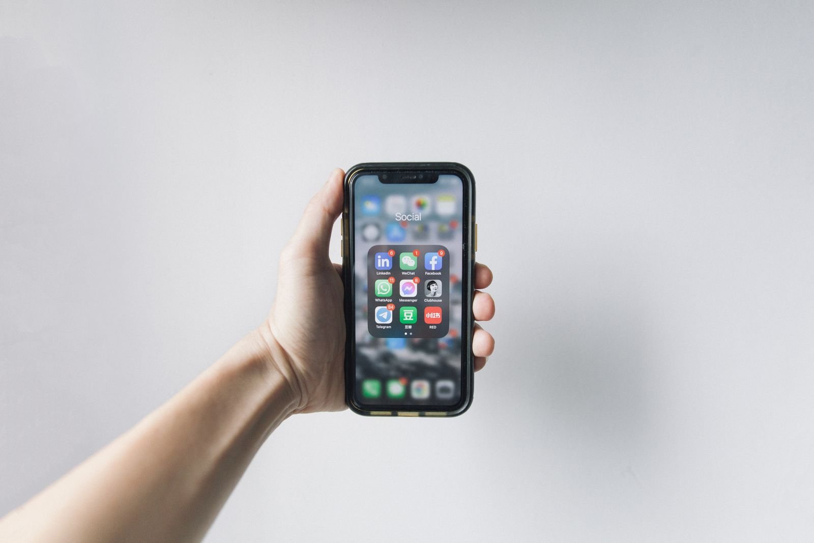 A hand holding a smartphone showing its home screen full of apps
