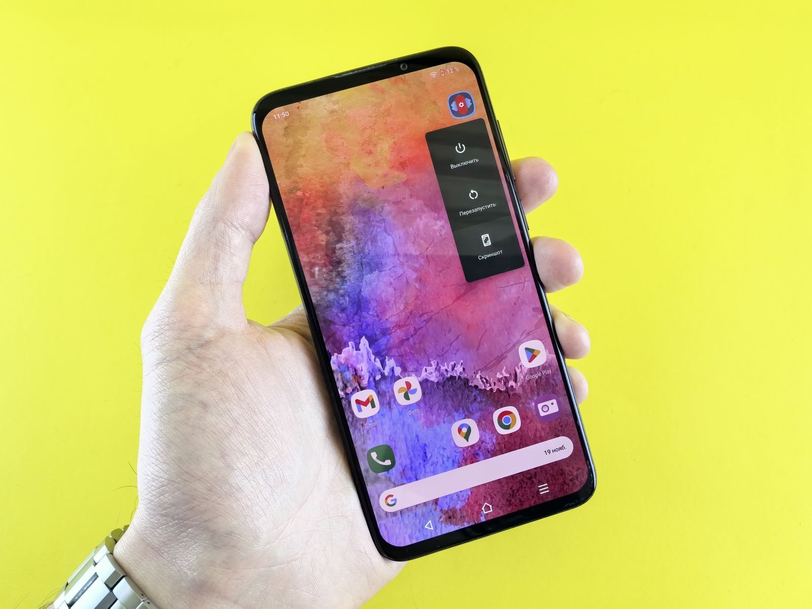 A hand holding an Android smartphone with a colourful wallpaper against a yellow background