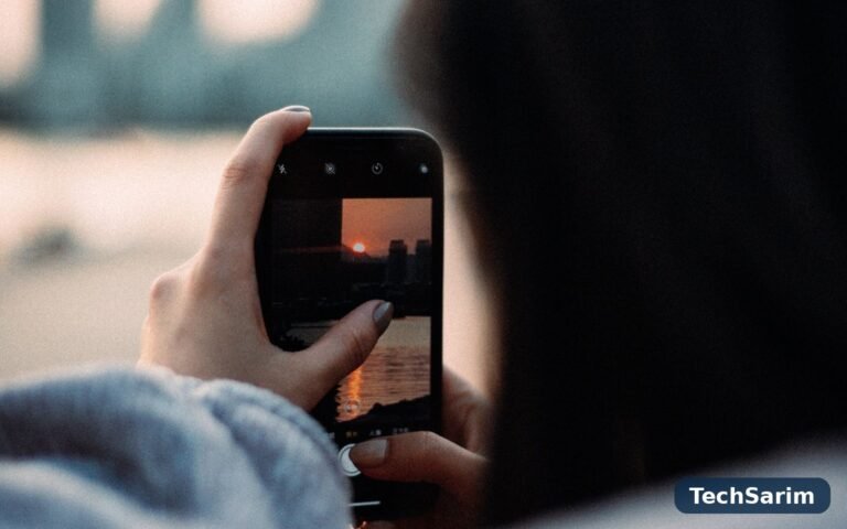 A person photographing a sunset over water with a smartphone