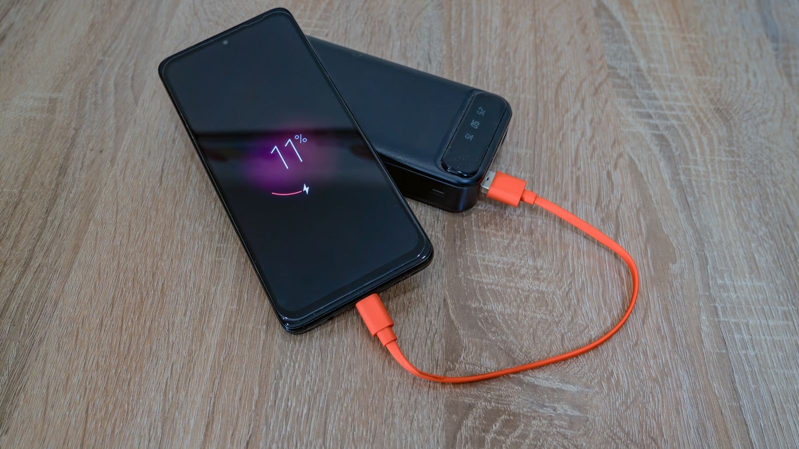 A smartphone at 11 percent battery charging from a power bank with an orange cable
