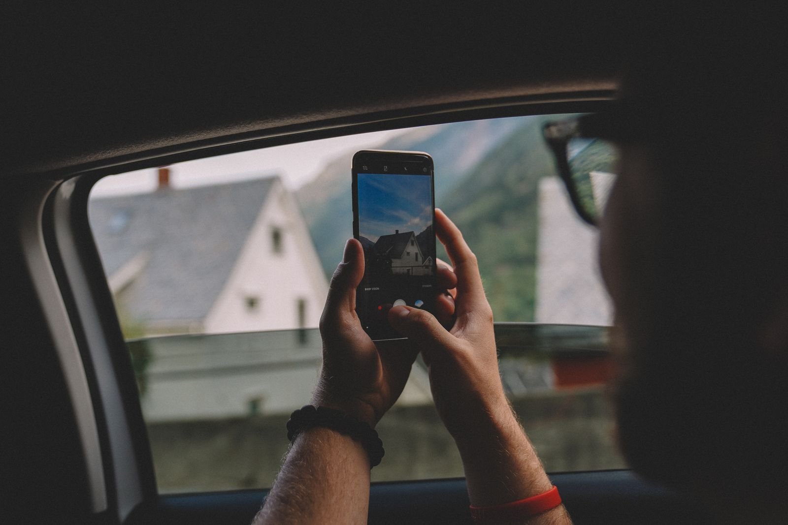 A person taking a photo of a house through a car window with a smartphone