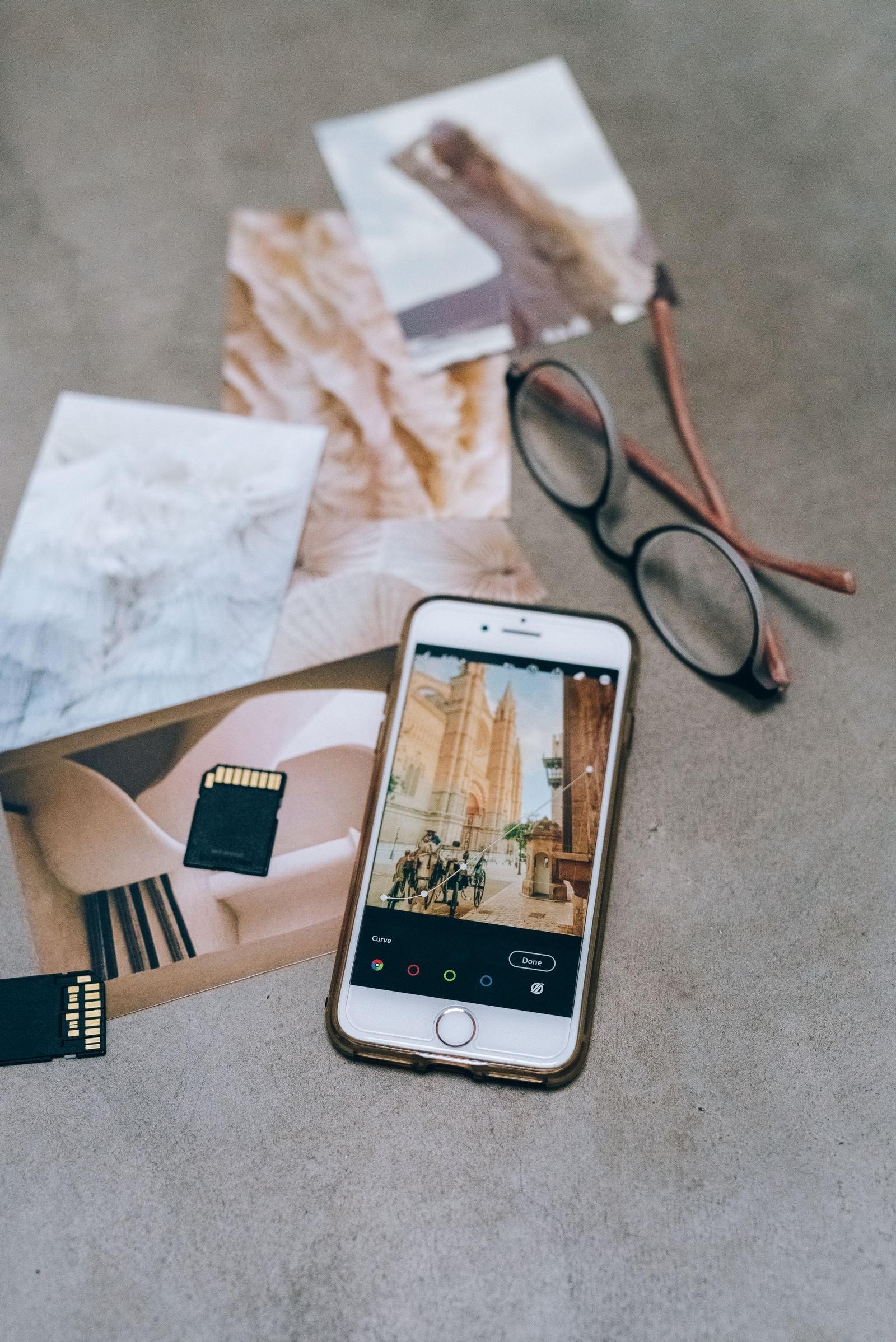 A smartphone editing a photo, lying beside printed photos and memory cards
