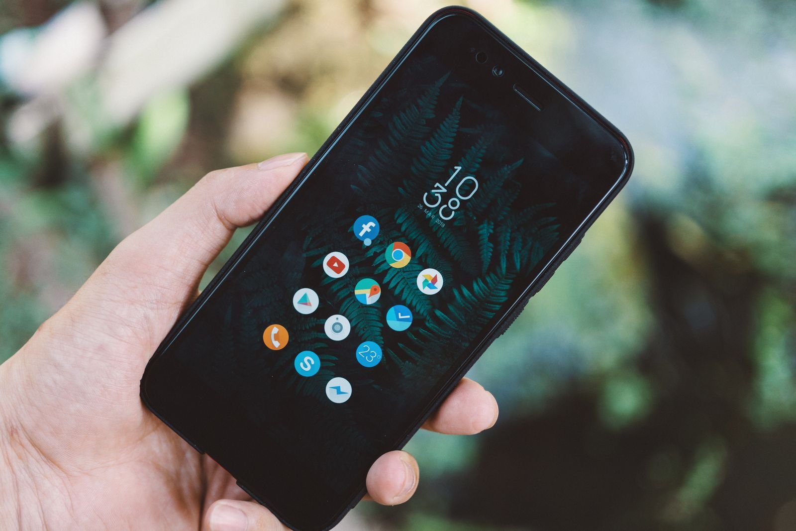A hand holding an Android phone showing a minimal home screen with round app icons