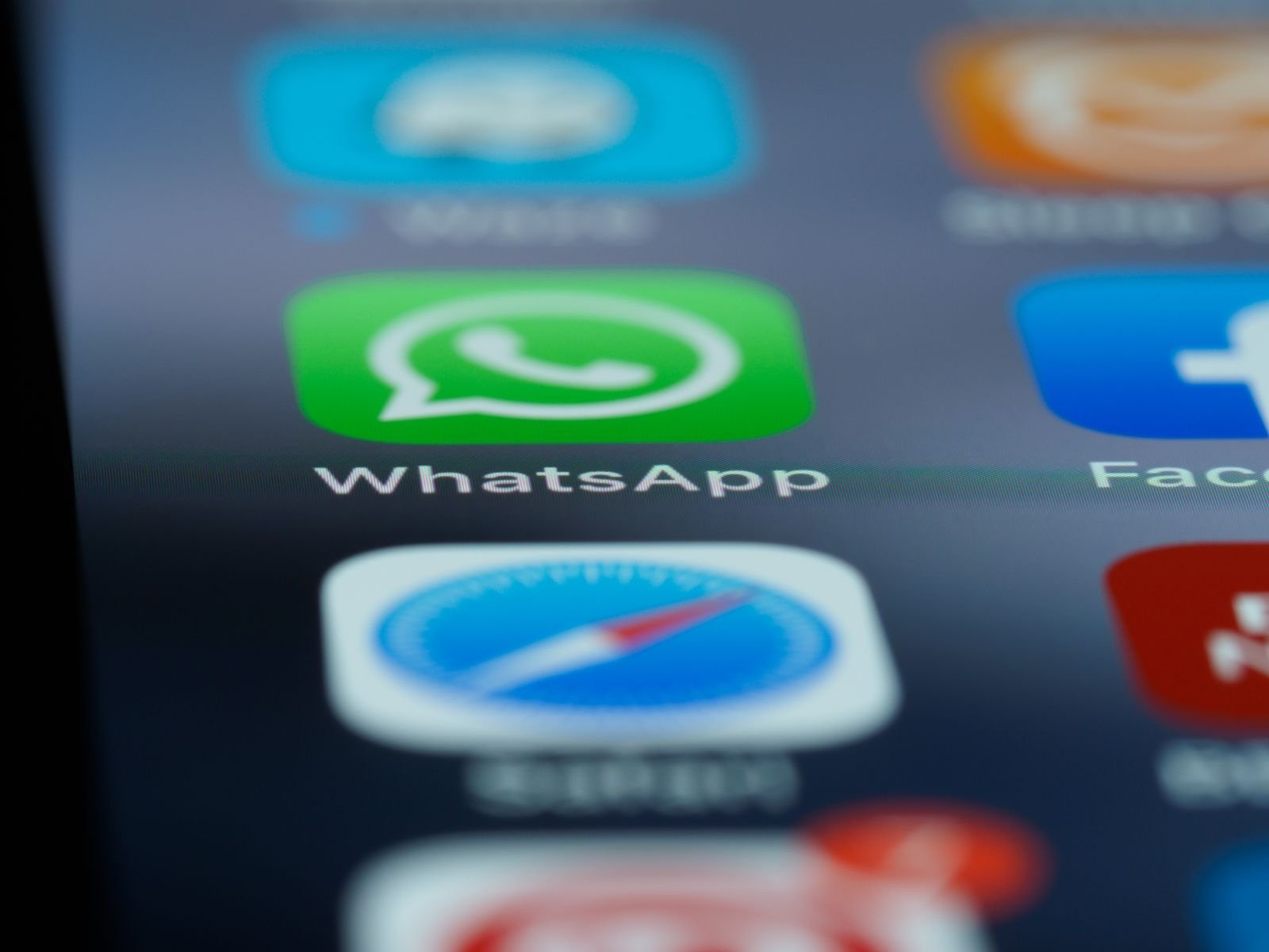 Close-up of the WhatsApp app icon on a phone screen next to Safari and Facebook