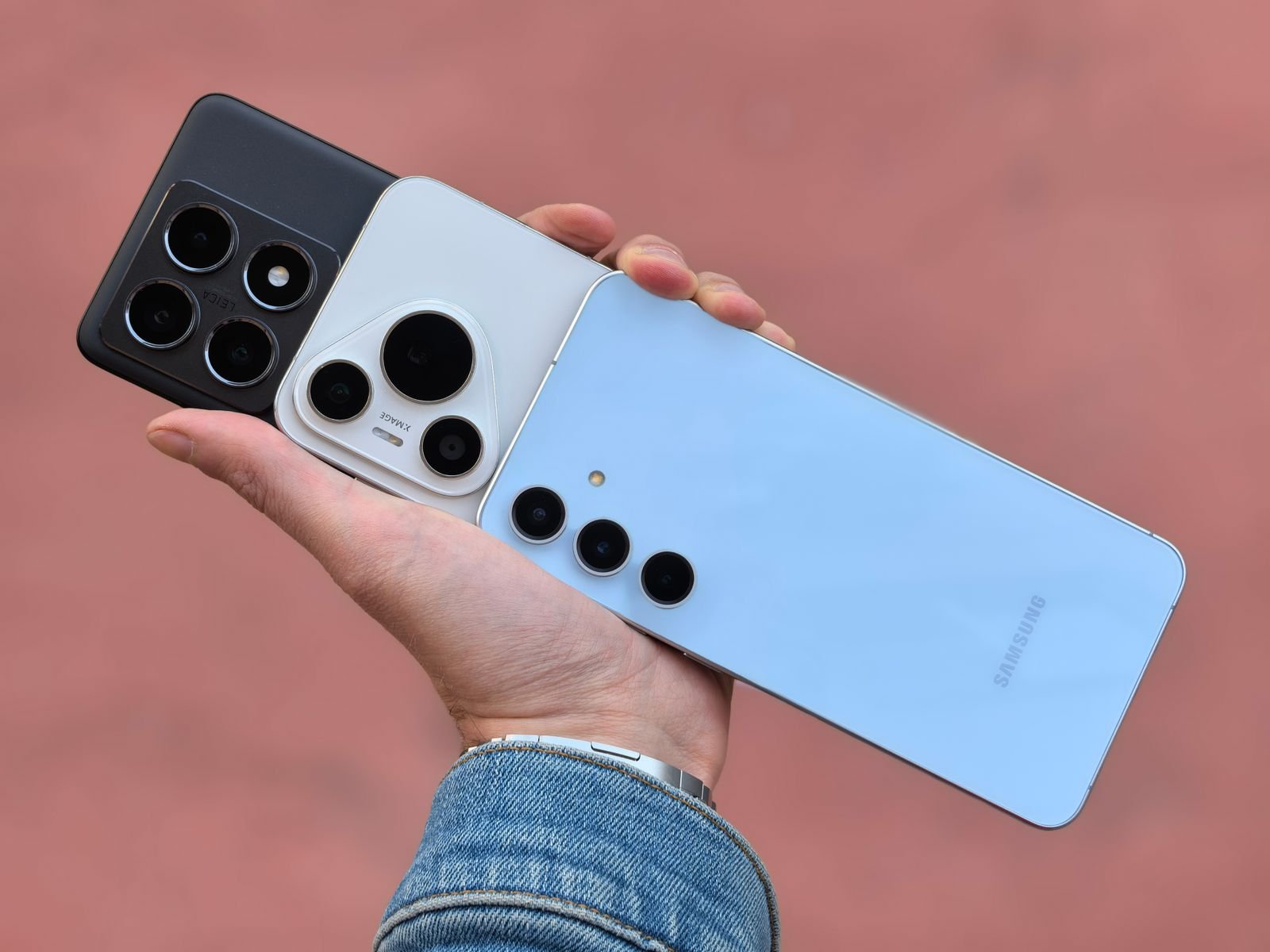 A hand holding three smartphones showing their different rear camera layouts