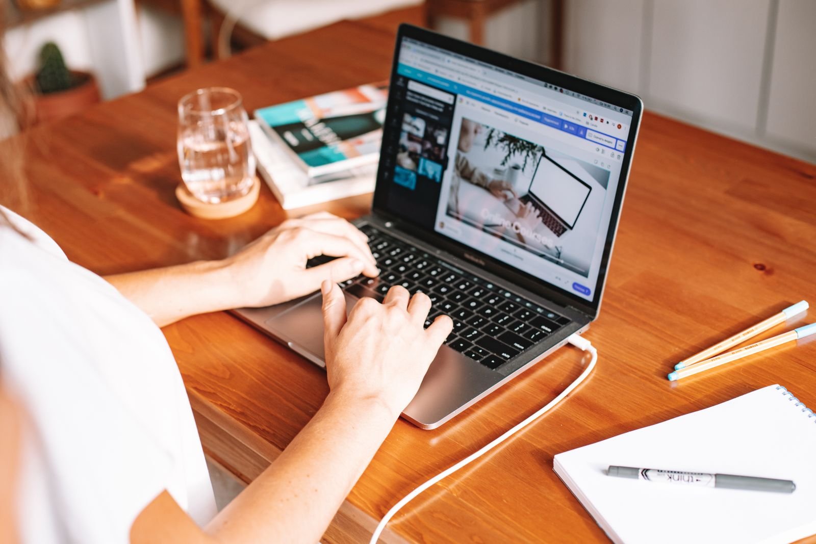 A woman typing on a laptop at a wooden table with books and a glass of water