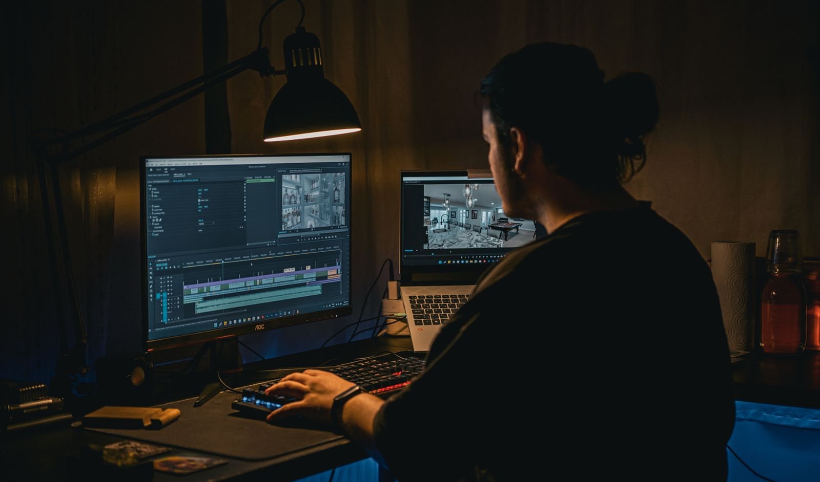 A man working at a computer in a dim room, editing video footage on screen