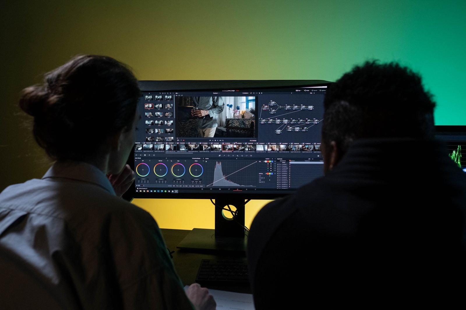 Two people video editing together at a desk with dual monitors