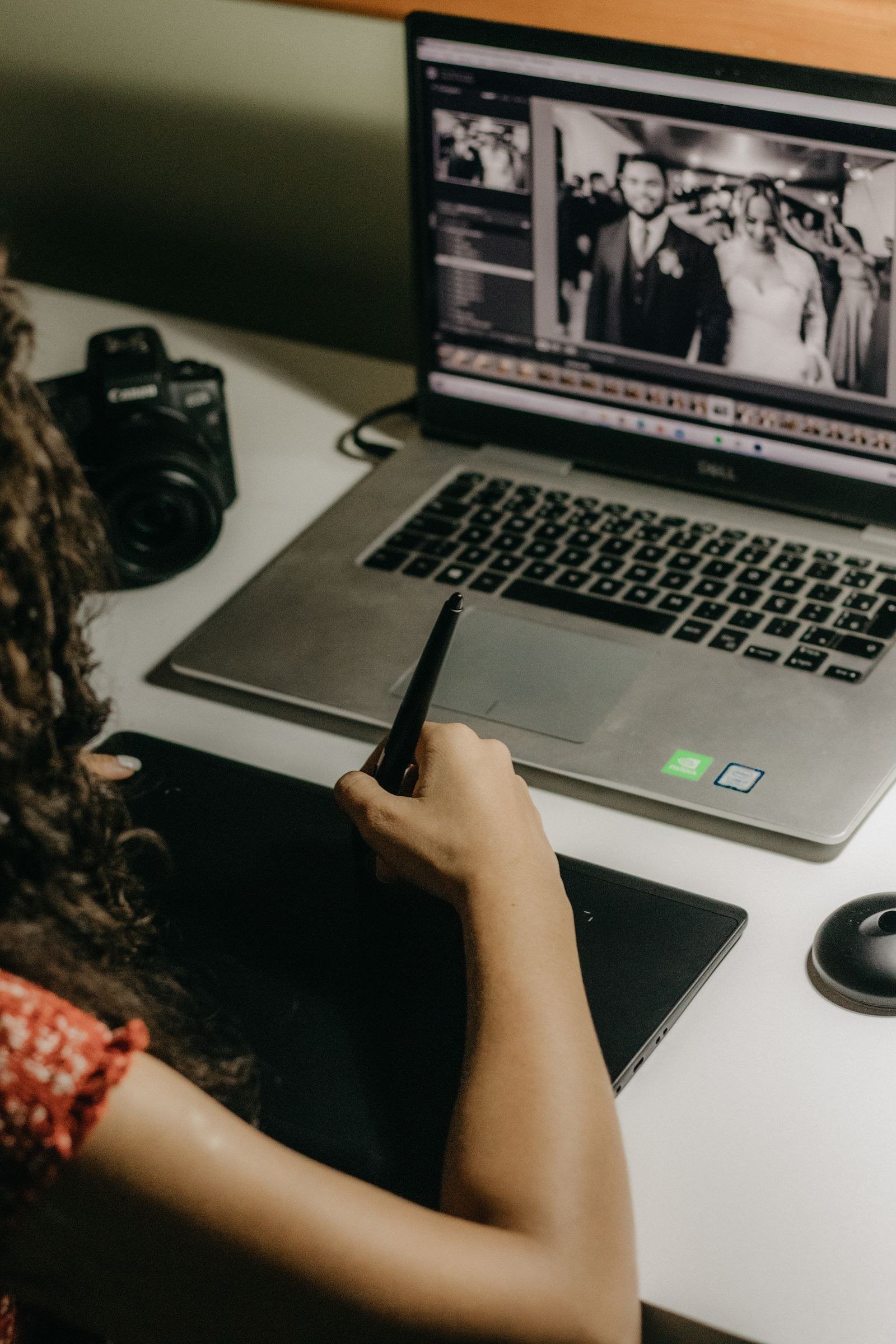 A photographer editing wedding photos on a laptop, using a graphics tablet for precise retouching