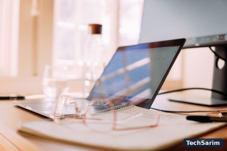 A bright home office desk with a laptop, external monitor, glasses and an open notebook, set up for focused work