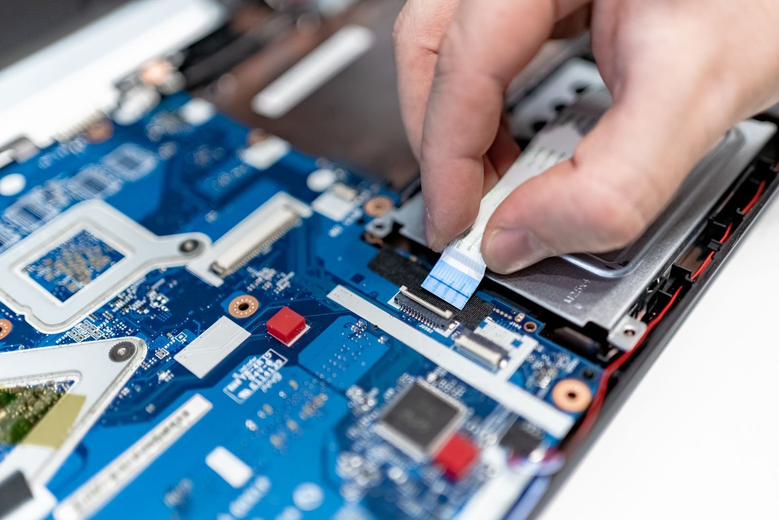 Close-up of fingers reseating a ribbon cable on the blue motherboard inside an opened laptop