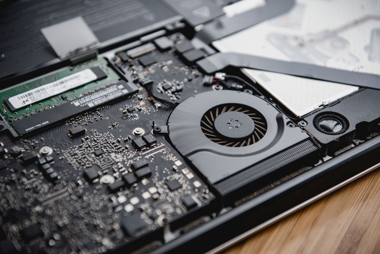 The inside of an opened laptop showing its cooling fan, motherboard and a stick of RAM