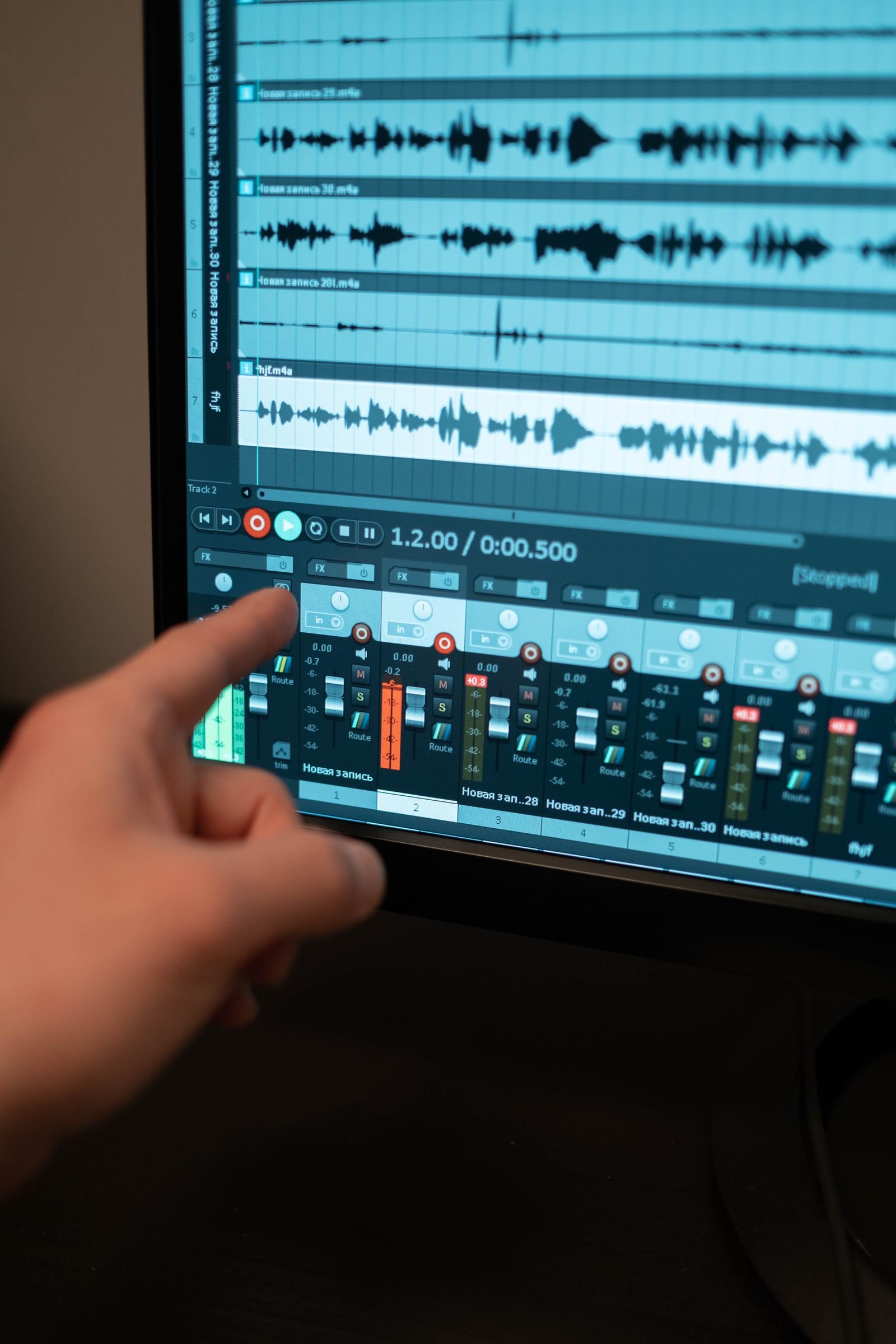 Close-up of a hand pointing at audio recording software on a monitor, with track waveforms, mixer faders and a red record button