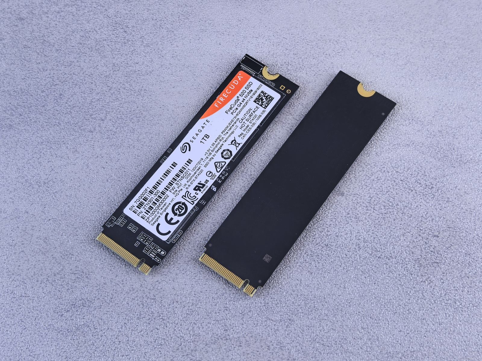 Two M.2 NVMe SSD sticks on a grey surface, one showing its label and gold connector