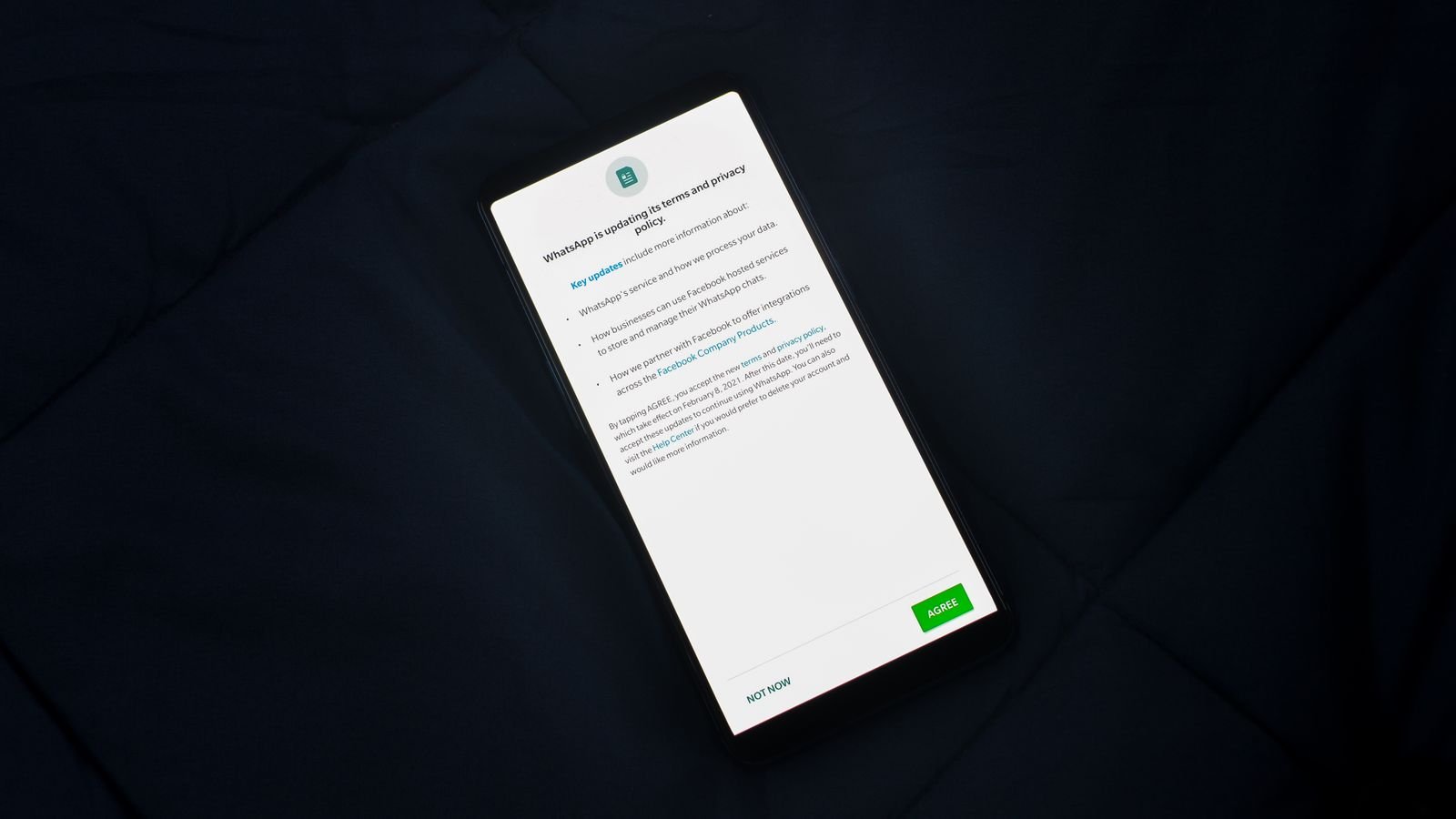 A smartphone lying on a dark fabric surface displaying a WhatsApp terms and privacy policy update with Agree and Not Now buttons
