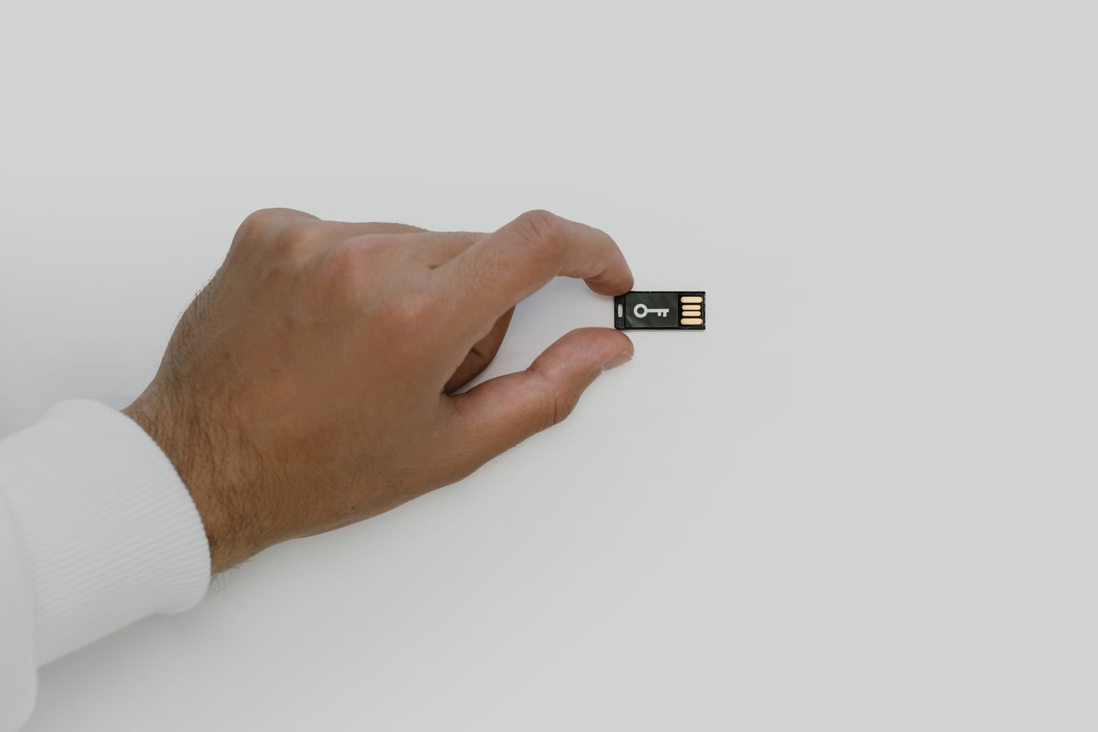 A hand holding a small black USB security key marked with a white key symbol against a plain white background