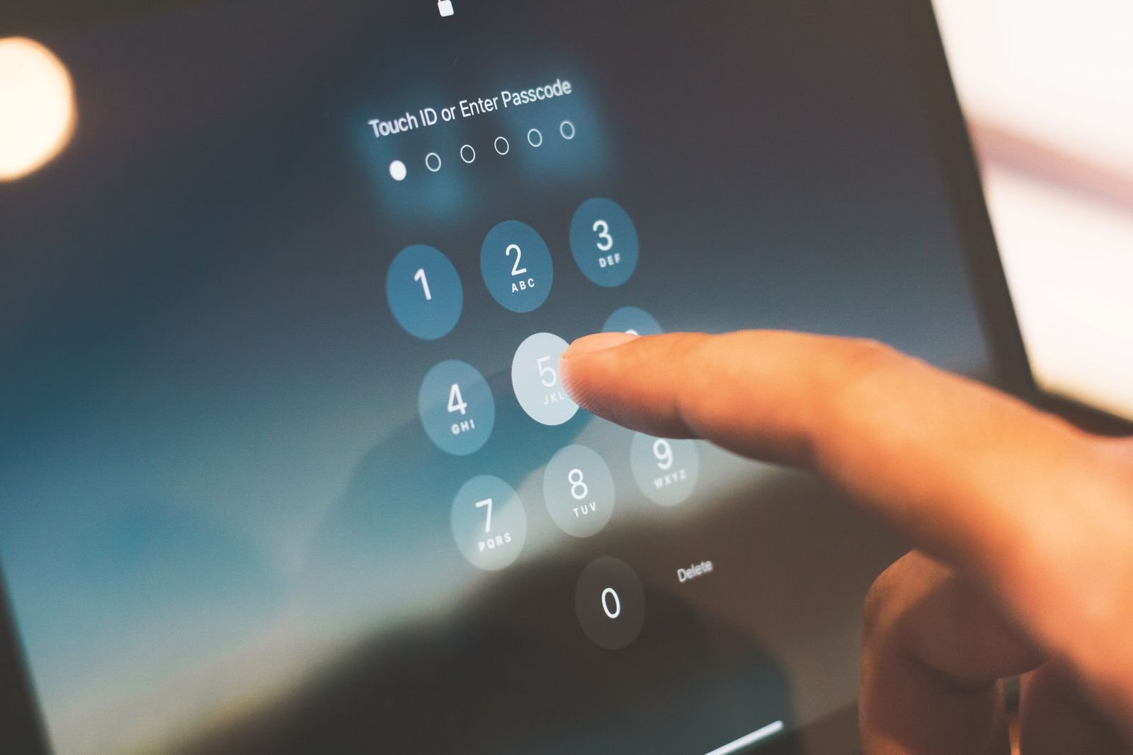 A finger entering a passcode on a tablet's numeric keypad below the words Touch ID or Enter Passcode