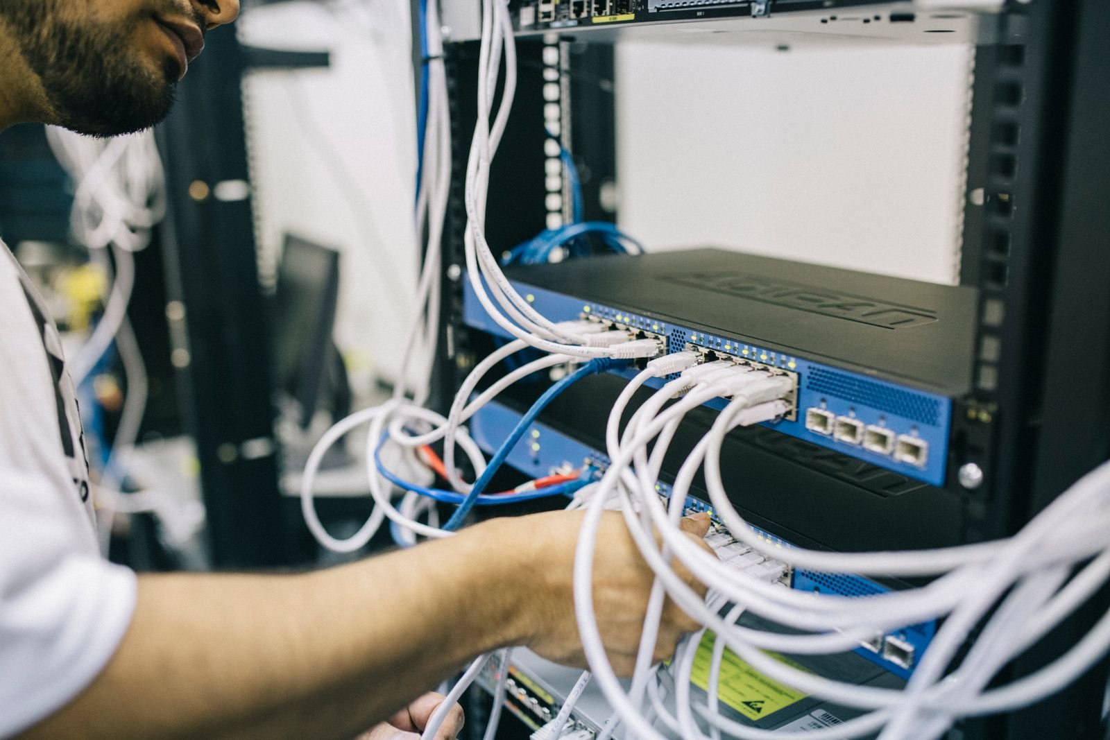 A technician plugging white Ethernet cables into a blue network switch mounted in a server rack