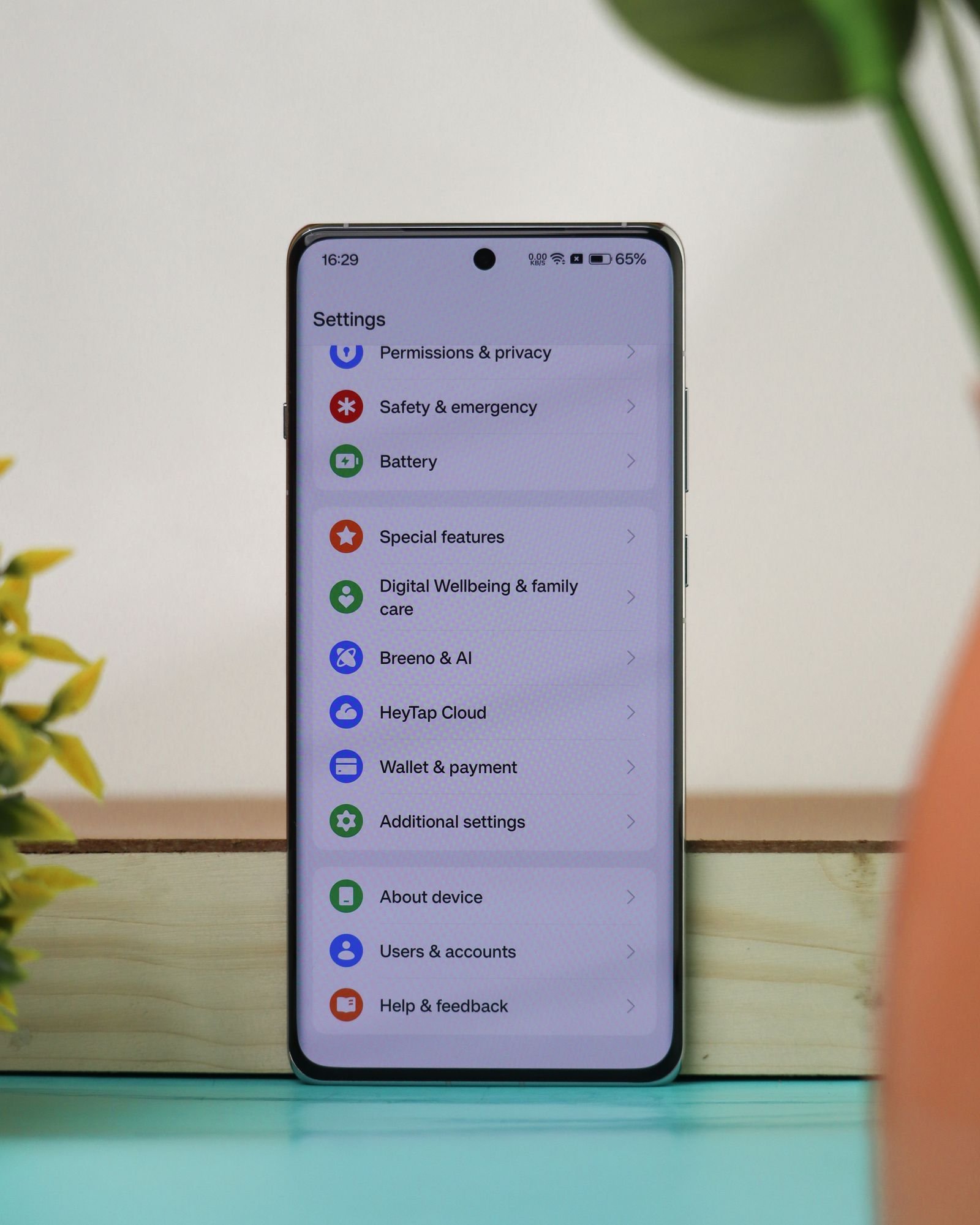 An Android smartphone standing on a desk showing its Settings menu, with Permissions and privacy near the top