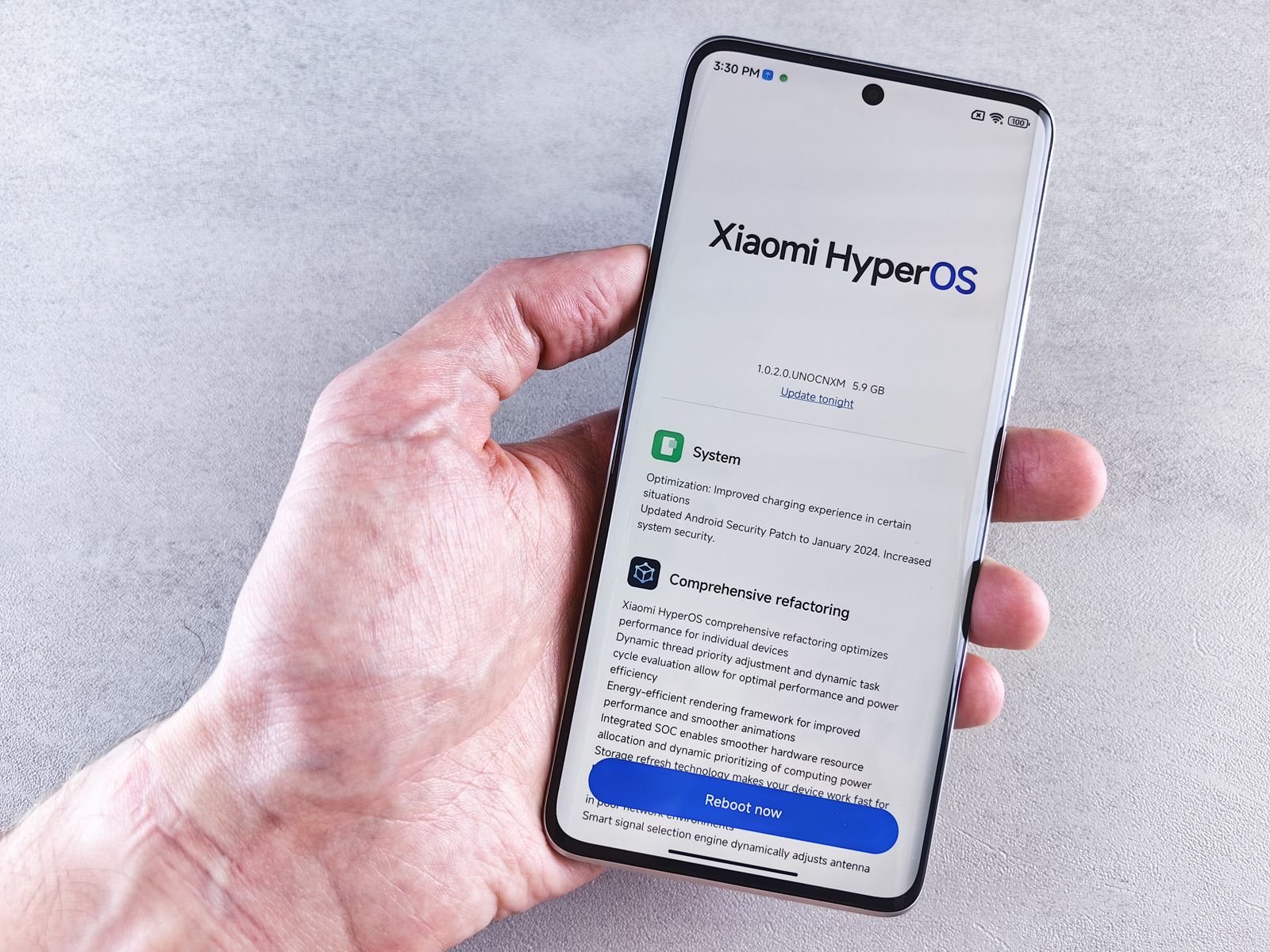 A hand holding a Xiaomi smartphone showing a HyperOS system update screen with an updated Android security patch listed