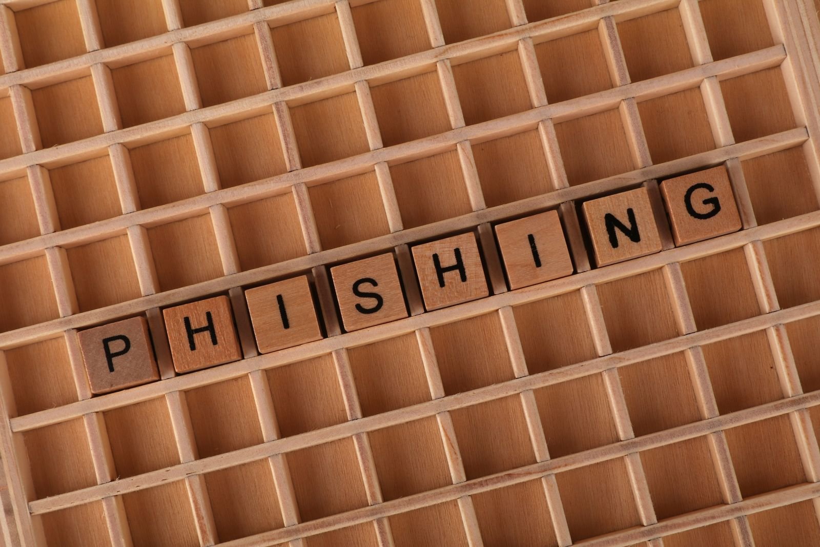 Wooden letter tiles spelling PHISHING laid in a row on a wooden letter tray