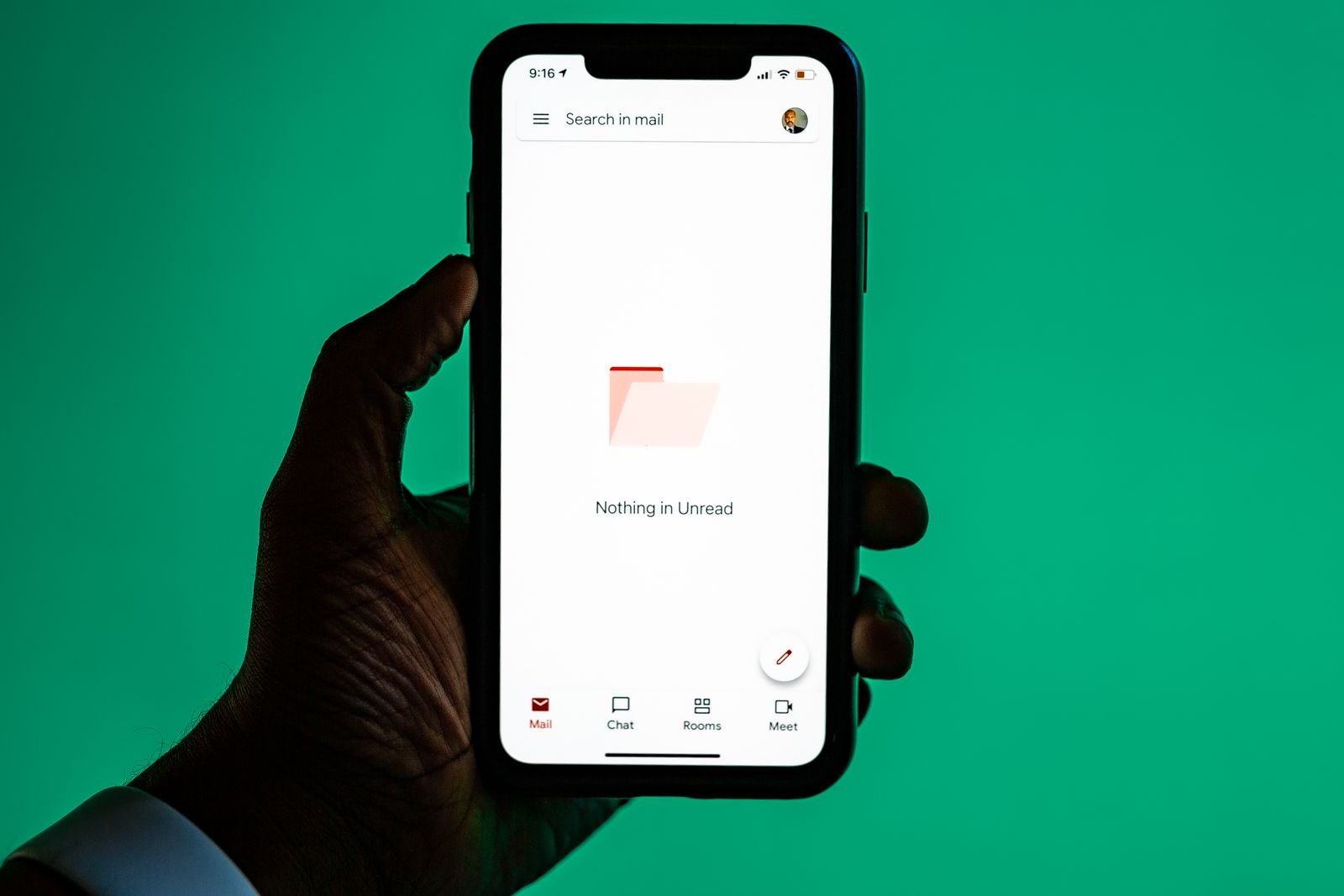 A hand holding a smartphone showing an email inbox screen against a solid green background