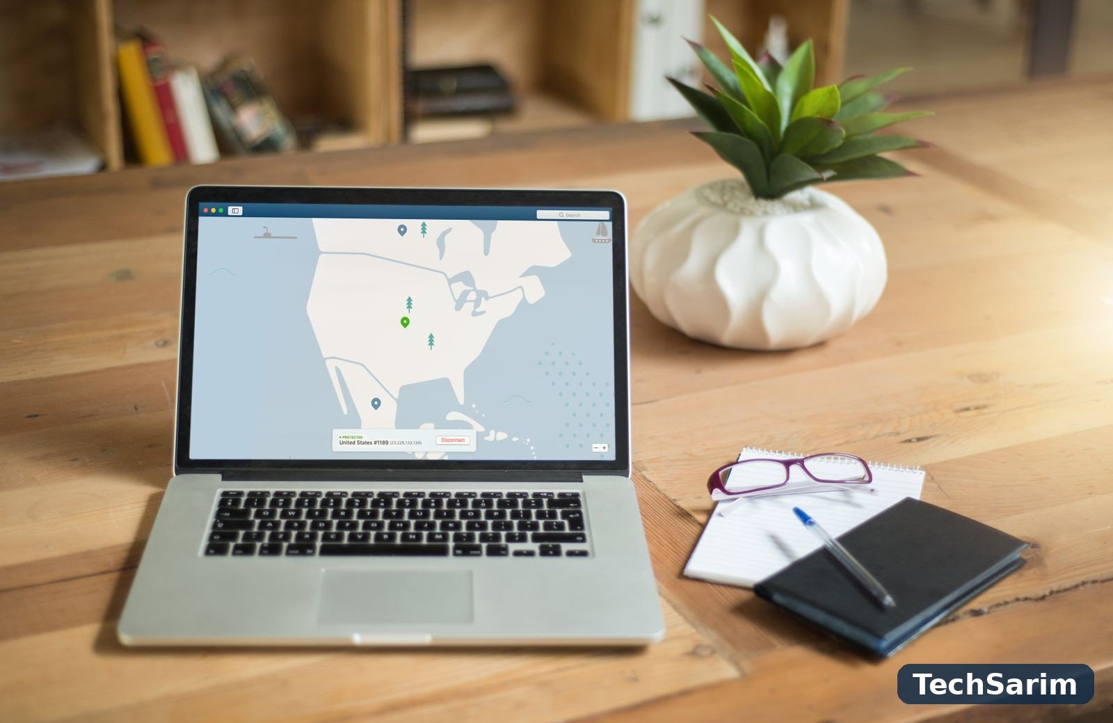 A laptop on a wooden desk displaying a VPN app's map with a protected United States connection, beside a potted succulent plant, a notebook and glasses
