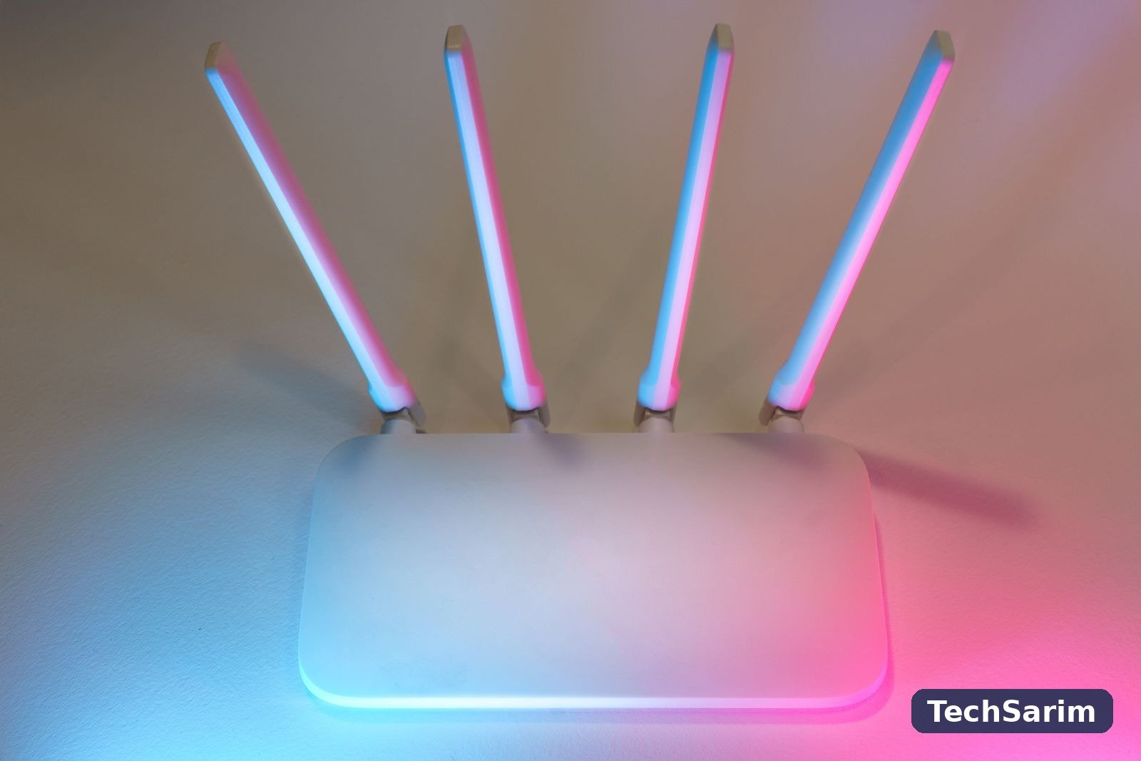 A white WiFi router with four tall antennas on a plain surface, lit by blue light on one side and pink light on the other