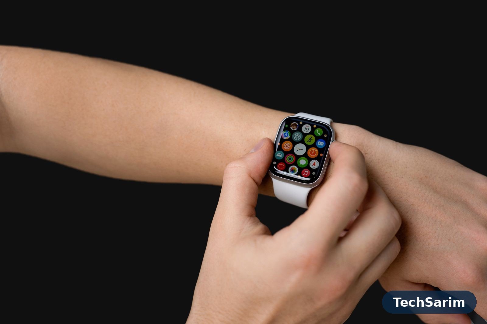 Close-up of a smartwatch with a white strap on a wrist against a black background, its screen showing a grid of colourful app icons