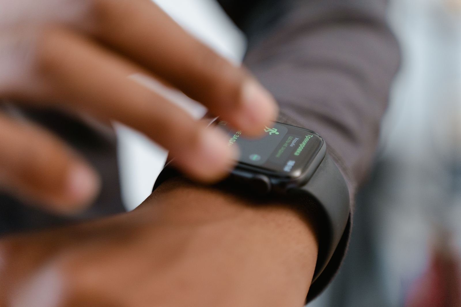 Close-up of a finger tapping the workout screen of a black smartwatch, which shows a green running figure icon