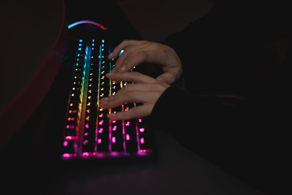 Close-up of hands typing on an RGB backlit mechanical keyboard in a dimly lit room