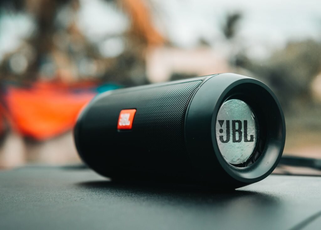 Close-up of a black cylindrical JBL portable speaker lying on its side outdoors, its end cap and logo in focus