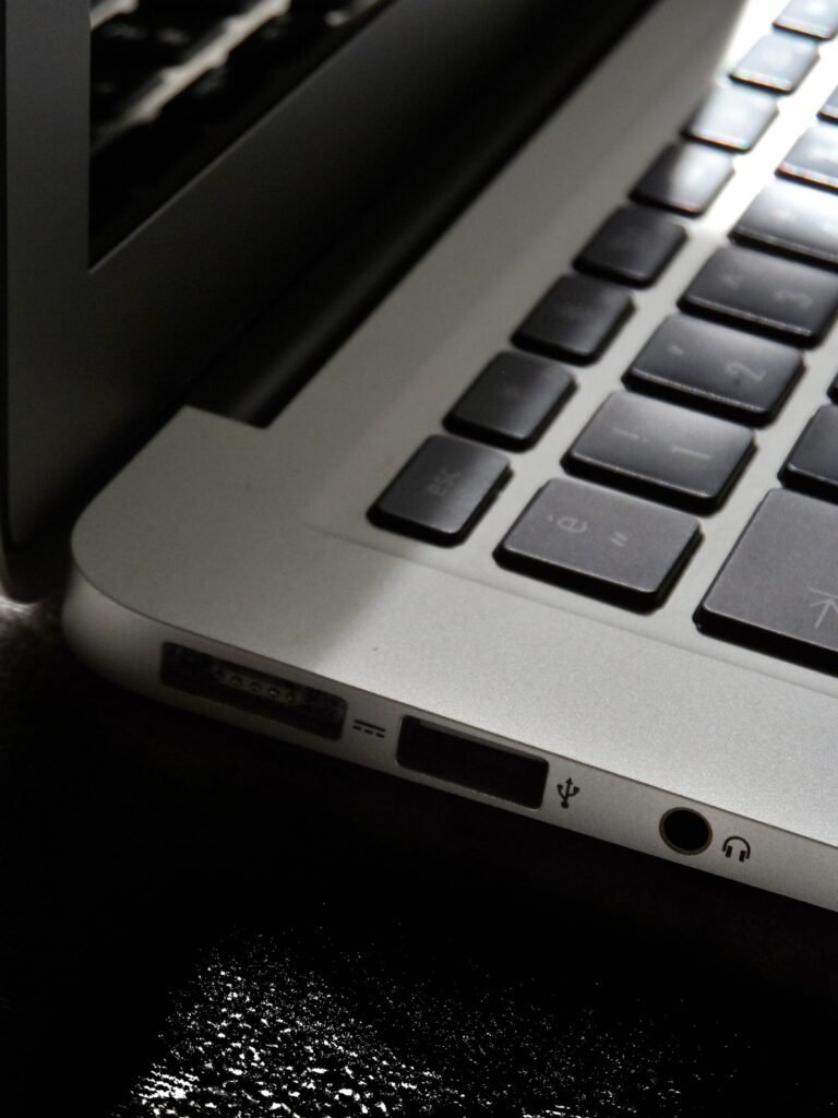 Close-up of the corner of a silver laptop showing part of its black keyboard and the charging, USB and headphone ports along its side