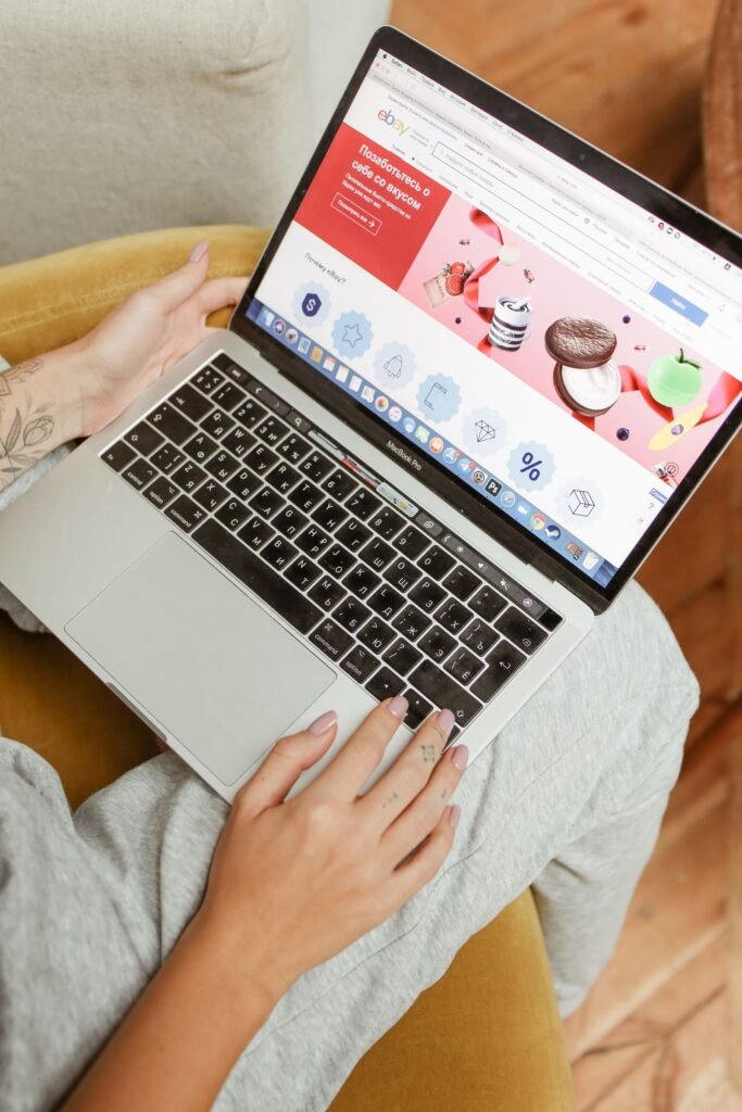 A person sitting on a sofa with a laptop on their lap, browsing a shopping website on its screen